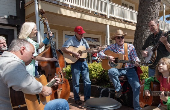 Musicians of all ages playing guitar, banjo, and upright bass together in an outdoor porch jam